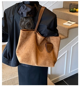 Detail of a large brown suede tote bag with a small magnetic charm on a matching strap