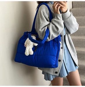 Royal blue quilted tote bag with white plush rabbit charm on a grey cardigan background