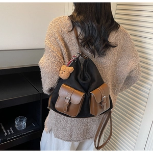 Detail of canvas underarm bag with leather flip pockets and plush bear charm accent
