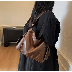 Detail of dark brown leather tote bag with side flap pockets shown on a shoulder