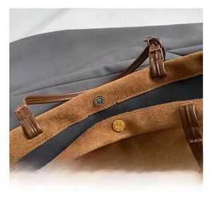 Close-up of brown suede tote bag featuring a golden magnetic closure and leather handle