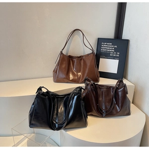 Three large shiny faux leather tote bags in brown, coffee, and black on a white stand