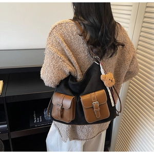 Detail view of black textured tote bag with brown pockets and cute plush bear charm