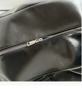 Close-up of premium smooth silver metal zipper on minimalist black leather tote bag