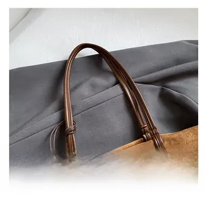 Detail of soft brown suede tote featuring dark leather handles and a side knot accent