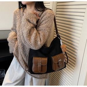 Detail of black canvas shoulder bag with brown leather trim and two buckle pockets