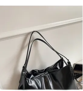 Detail of black glossy leather tote bag showing unique pleated texture and metal strap buckle