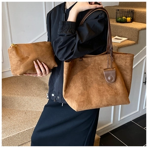 Detail of a brown suede tote bag and matching pouch held by a model on stairs