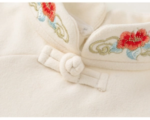 Detailed view of traditional Chinese embroidery and handmade button on a warm cream shirt