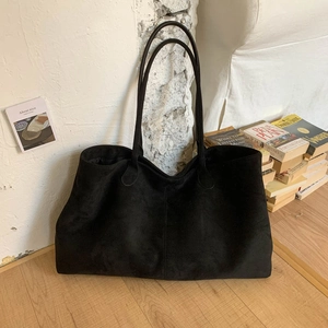 Detail view of large black suede tote bag placed on wooden floor with vintage books