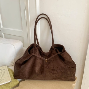 Close-up of deep brown suede tote bag with slim handles in a warm interior setting