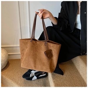 Close-up of large brown faux suede tote bag with dual handles and hanging charm