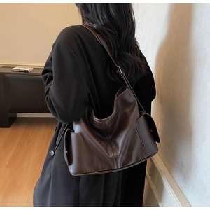 Detail of a large dark brown tote bag in matte PU leather worn by a model in a minimalist room