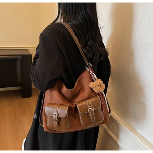 Brown suede tote bag with front flap pockets and a plush bear charm on a model