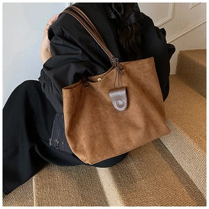 Close-up of brown suede tote bag with slim handles and decorative leather pendant