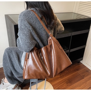 Detail of glossy brown tote bag with adjustable metal buckle and soft pleated leather