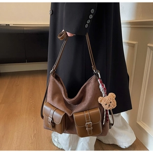 Detail of a brown suede hobo bag with front leather pockets and a plush bear pendant