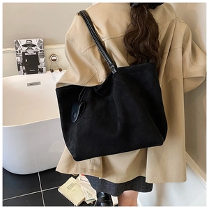 Macro detail of the black suede tote bag texture with long shoulder strap and charm