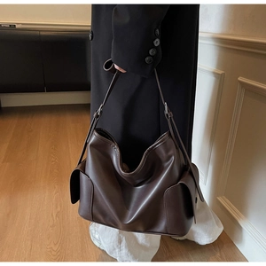 Detail view of brown leather tote bag showing matte texture and functional side pockets