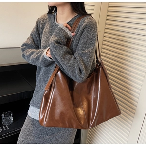 Detailed view of large brown glossy faux leather tote bag on a stylish shoulder