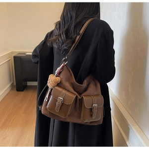 Close-up of deep brown suede tote bag with dual front pockets and plush bear charm