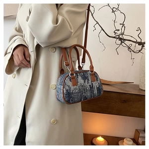 Close-up of a blue sequined boston bag styled with a beige trench coat and leather strap