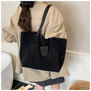 Close-up of black suede tote bag featuring unique knotted strap and leather pendant detail