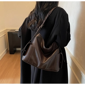 Detail view of large dark brown leather tote bag with wide strap on woman shoulder