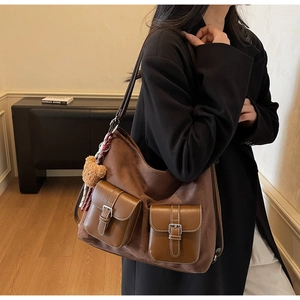 Detail of coffee brown suede tote bag with leather flap pockets and bear charm