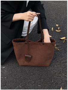 Detail of a large brown suede tote bag featuring a leather shield pendant in autumn setting