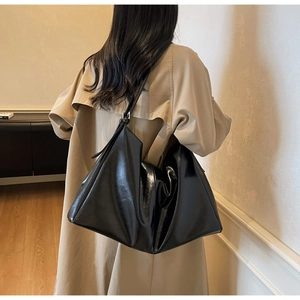 Detail of black faux leather tote bag with metallic buckle strap on model shoulder