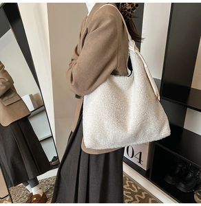 Detailed view of white Sherpa tote bag with leather strap worn by model in brown blazer