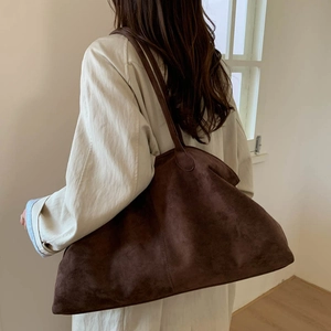 Detailed back view of a dark brown suede tote bag worn by a model in a minimalist room