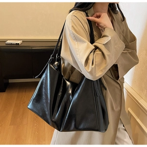 Detail of a black glossy leather tote bag showing large capacity and adjustable buckles