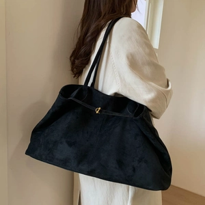 Detail view of large black suede tote bag with golden metal buckle on model shoulder