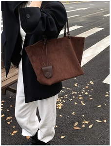 Detail of dark brown suede tote bag with long leather strap in autumn urban street setting