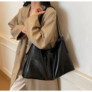 Close-up of a black leather tote bag worn with a stylish trench coat in an indoor setting