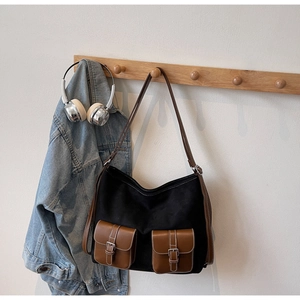 Detail of canvas tote bag with brown leather front pockets and silver buckles