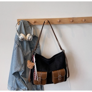Detail of black canvas shoulder bag featuring brown leather pockets and a cute bear charm