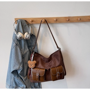 Detail view of retro brown suede tote bag with leather pockets and bear charm hanging on a hook