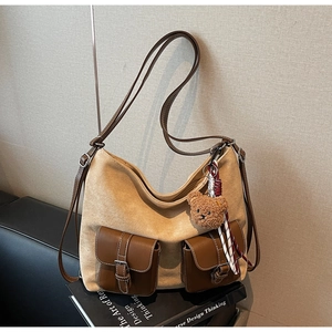 Detail view of beige suede shoulder bag with dual brown leather pockets and plush bear charm