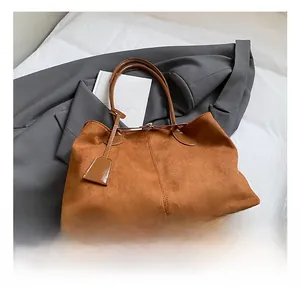 Détail d'un sac cabas en daim marron avec coutures apparentes et étiquette décorative