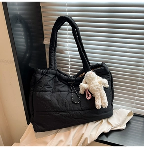 Detail of black puffer tote bag with quilted texture, drawstring and plush bunny charm