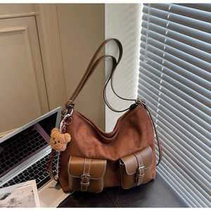 Detail of brown suede tote bag with dual buckled pockets and cute plush bear charm
