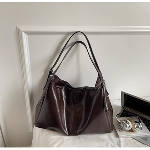 Detail of dark brown tote bag with adjustable straps next to a laptop and headphones