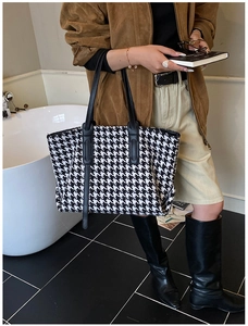 Detail of houndstooth tote bag with black leather straps shown in lifestyle setting