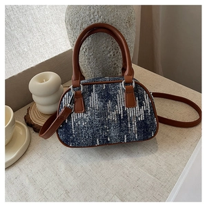 Detail of blue denim sequins handbag with brown strap on a beige textured surface