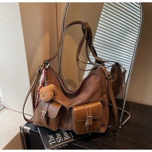 Detail of a brown suede hobo bag with front leather pockets and a cute teddy bear charm