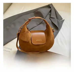 Close-up of brown suede hobo bag with leaf charm on a grey blazer background