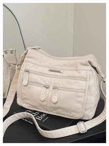 Close-up of beige soft leather crossbody bag featuring multiple zipper pockets and texture